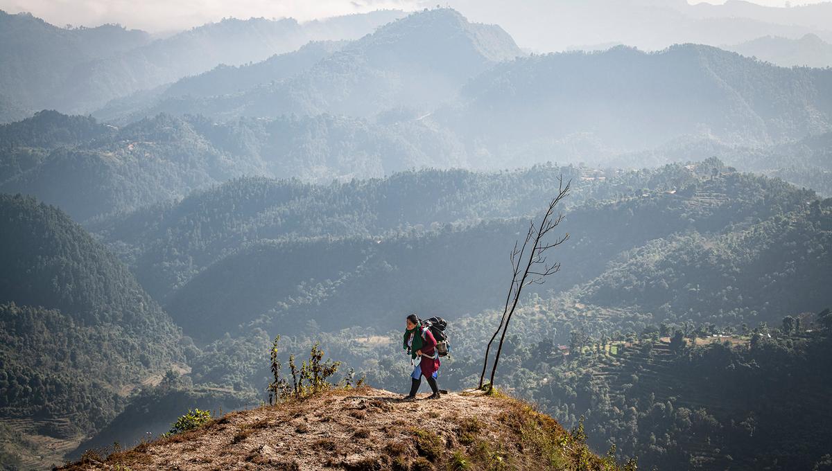 A hiker with a large backpack on a ridge above misty mountains.